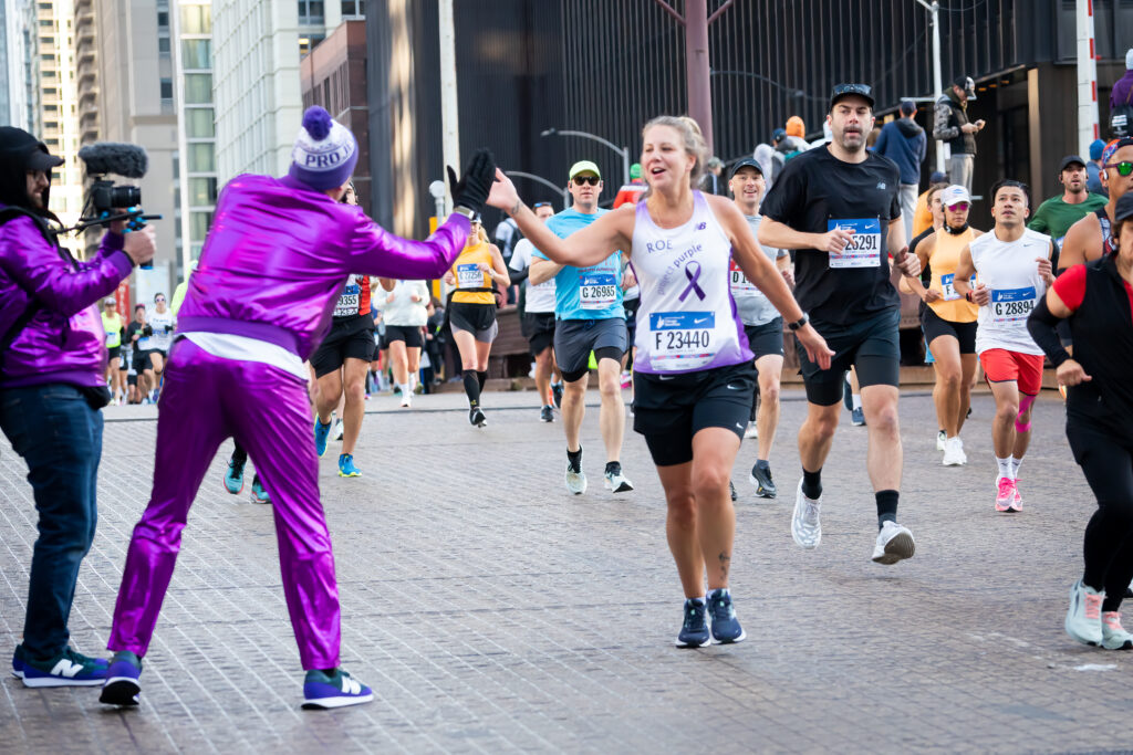 Chicago Marathon runner in Project Purple singlet high-fiving Project Purple founder and CEO Dino Verrelli running over a bridge.