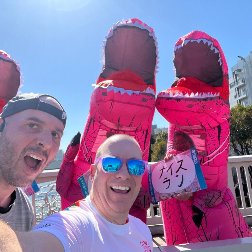Project Purple runners run past spectators in pink dinosaur costumes during the Tokyo Marathon